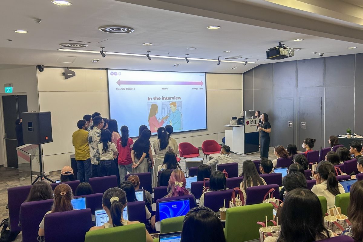 A packed RMIT room watching students role-play an interview beside a presentation screen