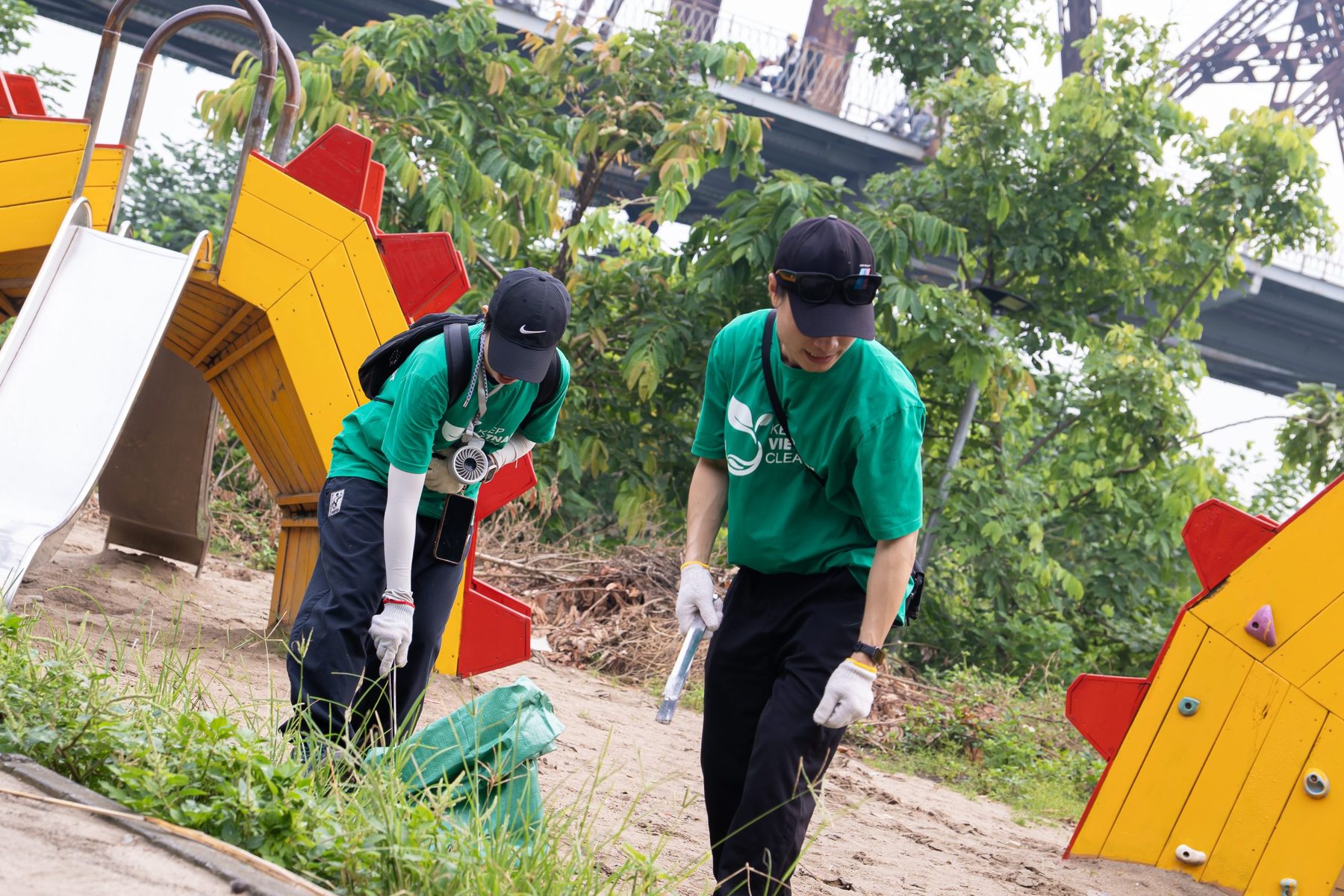 Two Keep Vietnam Clean volunteers collecting waste beside a playground
